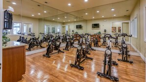 Une salle de sport équipée de plusieurs vélos d’appartement disposés en rangées, d’un grand mur miroir et d’un plancher en bois.