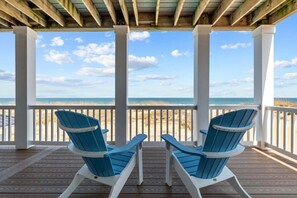Une terrasse en bois avec deux chaises Adirondack bleues, donnant sur la plage.
