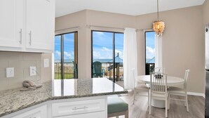 A modern kitchen with white cabinets, a granite countertop, and a dining area with a round table and chairs. - Beachfront 1BR @ Phoenix V • Sleeps 4 • Pools, Hot Tub & Pirate Splash Pad (Orange Beach)
