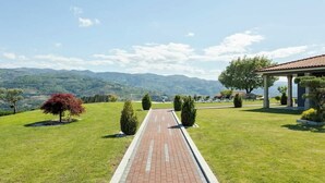 A paved pathway leading to a building with a red-tiled roof, surrounded by green grass and trees, with a mountainous backdrop. - HostWise - Douro Villa - Suite Teixeira Pascoares (Santa Marinha do Zêzere)
