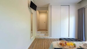A modern hotel room with a wooden floor, a bed with a blue bedspread, a breakfast tray on the bed, a TV mounted on the wall, and a door leading to a bathroom. - HostWise - Douro Villa - Suite Teixeira Pascoares (Santa Marinha do Zêzere)