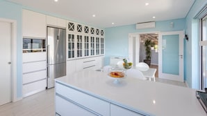 Une cuisine moderne avec des meubles blancs, un réfrigérateur en acier inoxydable et un îlot central sur lequel se trouve un saladier en verre rempli de fruits.