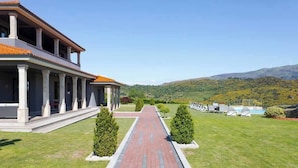 Un bâtiment doté d’une galerie couverte menant à un espace piscine, le tout entouré de pelouses bien entretenues et d’un paysage vallonné.