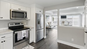 A modern kitchen with stainless steel appliances, white cabinetry, and a view to a living area. - Canandaigua Lakefront | Dock | Fire Pit | Kayaks (Rushville)