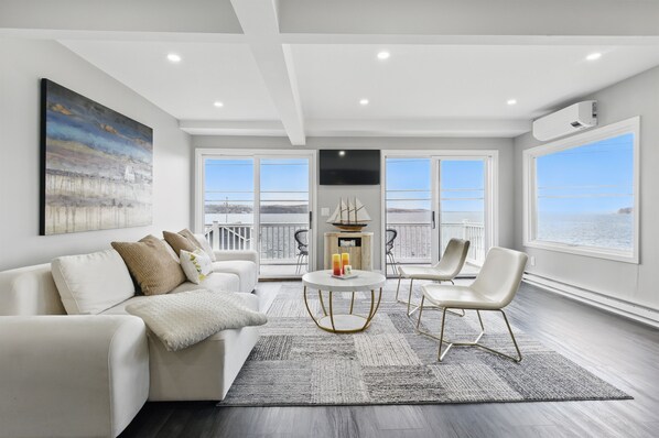 Een moderne woonkamer met een witte bank, een ronde salontafel en uitzicht op de zee door grote ramen.