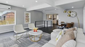 A spacious living area with a white sofa, a round coffee table, and a dining table with chairs. A staircase leads to an upper floor, and a large window provides a view of the outside. - Canandaigua Lakefront | Dock | Fire Pit | Kayaks (Rushville)