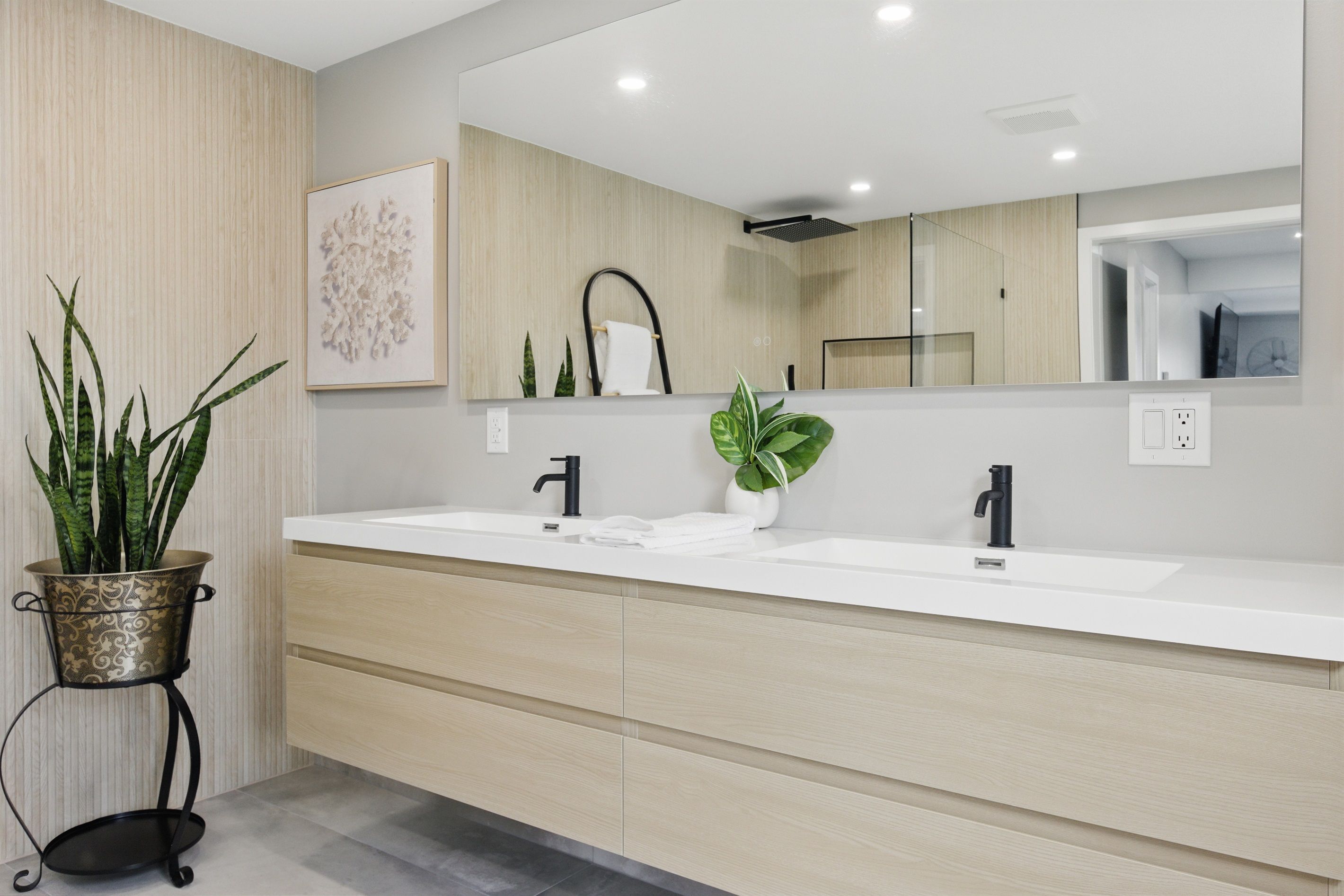 Une salle de bain moderne avec un double vasque, un grand miroir et une plante en pot.