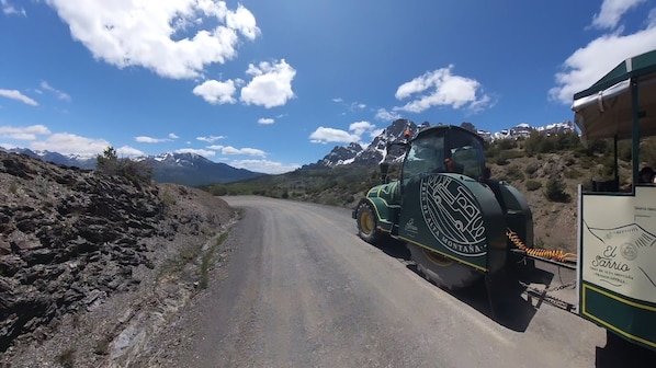 Un vehículo verde y amarillo sobre un camino de tierra, con montañas al fondo.