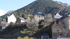 A stone building with a steep roof, surrounded by trees and a mountain in the background.
