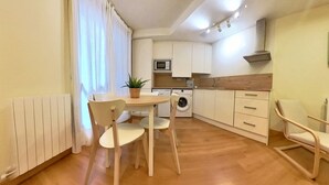A compact kitchen with a dining area, including a table, chairs, a washing machine, and a microwave.