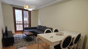 A living area with a sofa, a dining table with chairs, a TV stand, and a patterned rug.