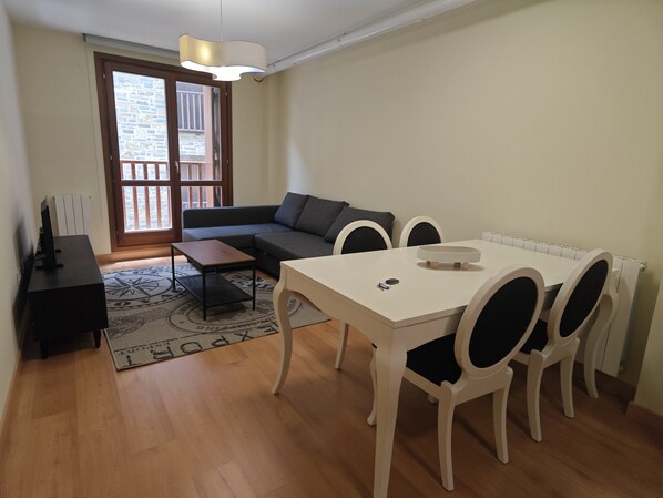 A living area with a sofa, a dining table with chairs, a TV stand, and a patterned rug.