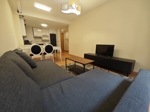 Olohuoneessa on sohva, sohvapöytä, televisio ja taustalla näkyy keittiö.
