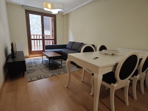 Ein modernes Wohnzimmer mit einer Couch, einem Esstisch mit StĂŒhlen, einem Fernseher und einem gemusterten Teppich.