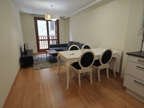 A compact living space with a dining table, chairs, a sofa, a TV, and a radiator.