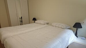 A bedroom with a bed, two bedside lamps, a nightstand, and a wardrobe.