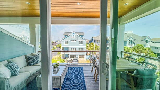 A balcony with a view of a large house, a dining table, and a sofa.
