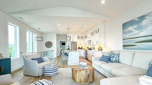 A spacious living room with a large sofa, a coffee table, and a dining area with white cabinetry.