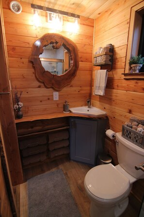 Compact bathroom with a white toilet, wooden vanity, and ornate mirror.
