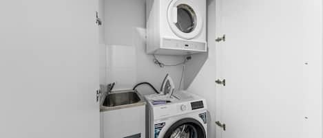 Un lavadero pequeño con lavadora de carga frontal, secadora empotrada y un lavabo.