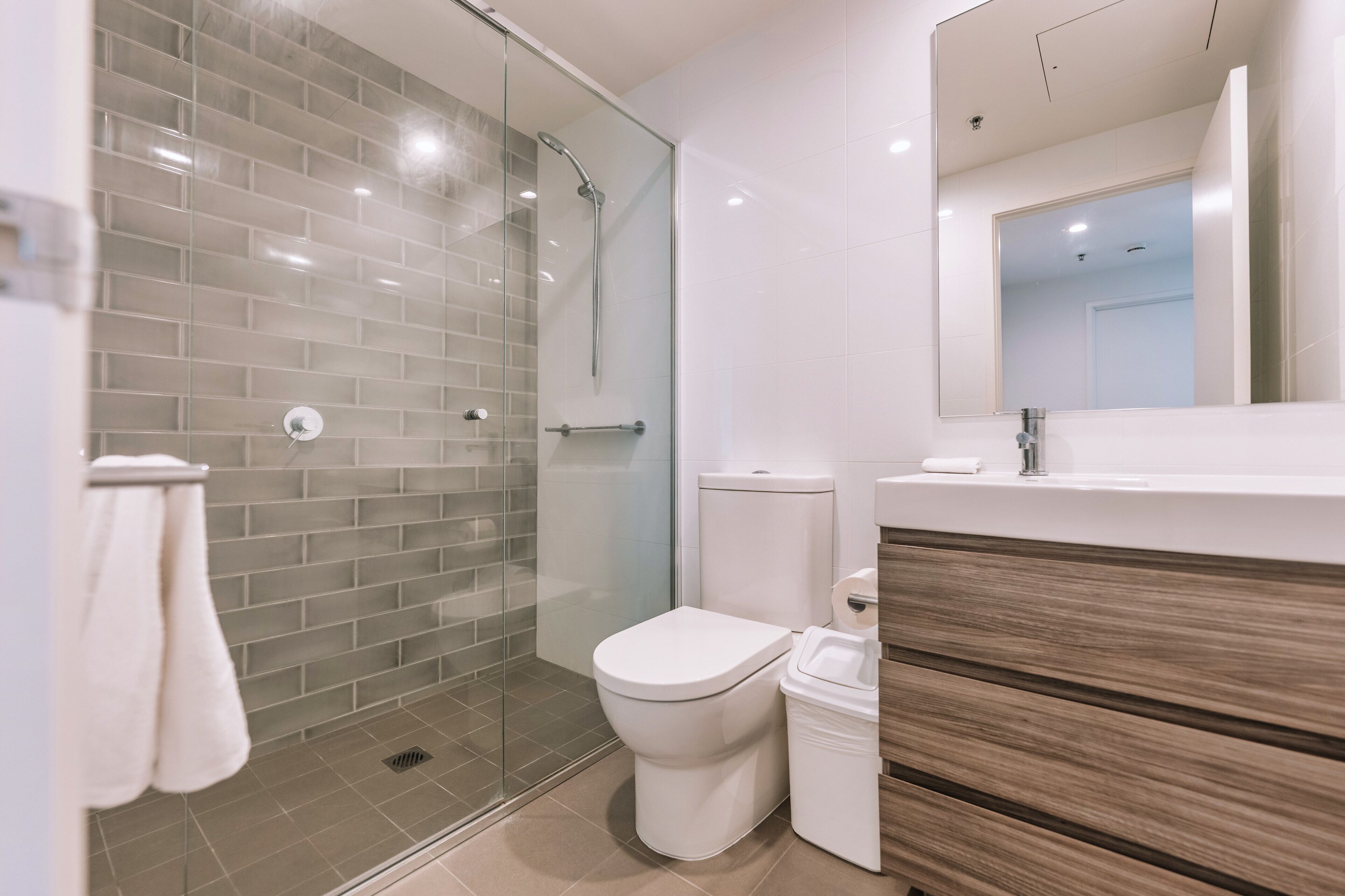 A modern bathroom with a glass shower enclosure, a white toilet, and a wooden vanity.