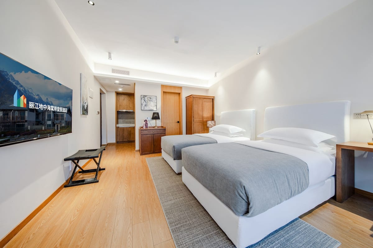 Una habitación de hotel moderna con dos camas, piso de madera, un ventanal y vista a un paisaje urbano.