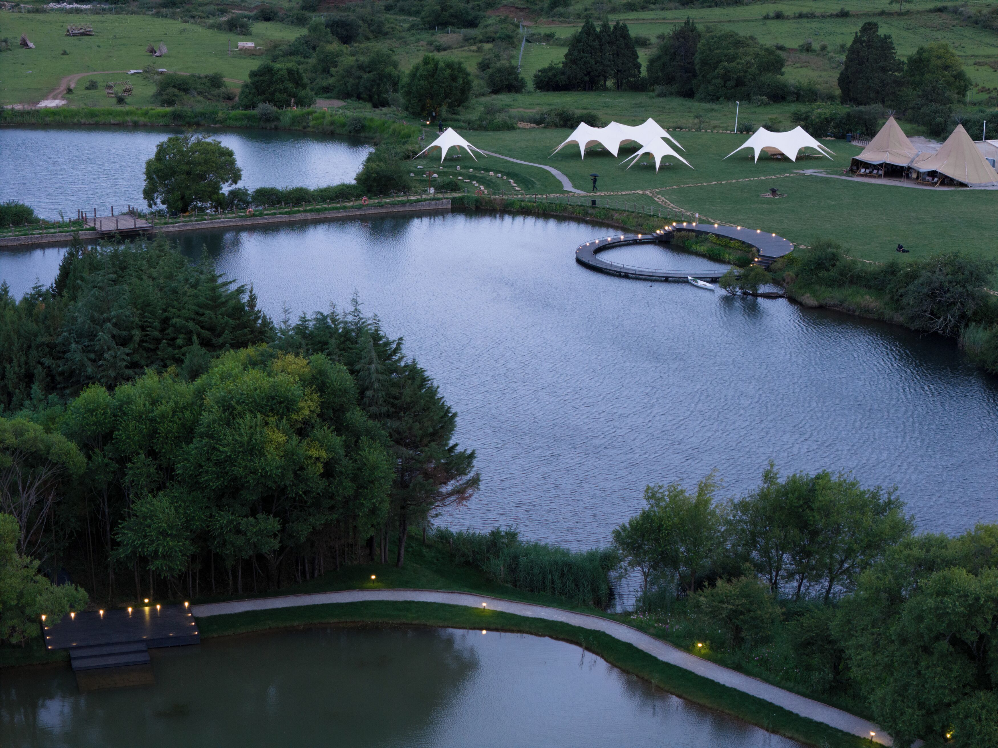 A lakeside view with a walking path, tents, and a dock.