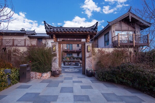 Una entrada de arquitectura china tradicional con techo de tejas, vigas de madera y un camino de piedra que conduce a un patio.