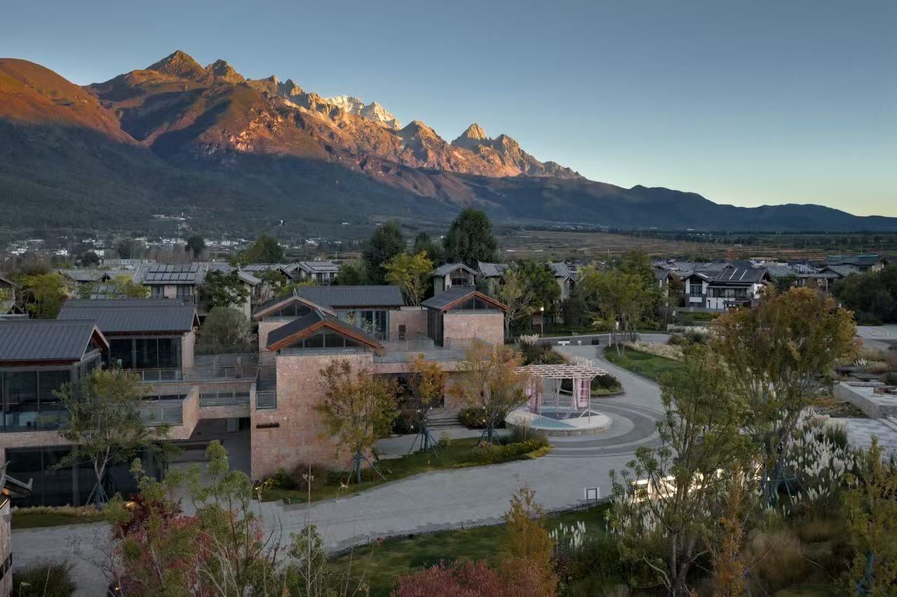 A residential area with modern houses, a central gazebo, and a mountain range in the background.