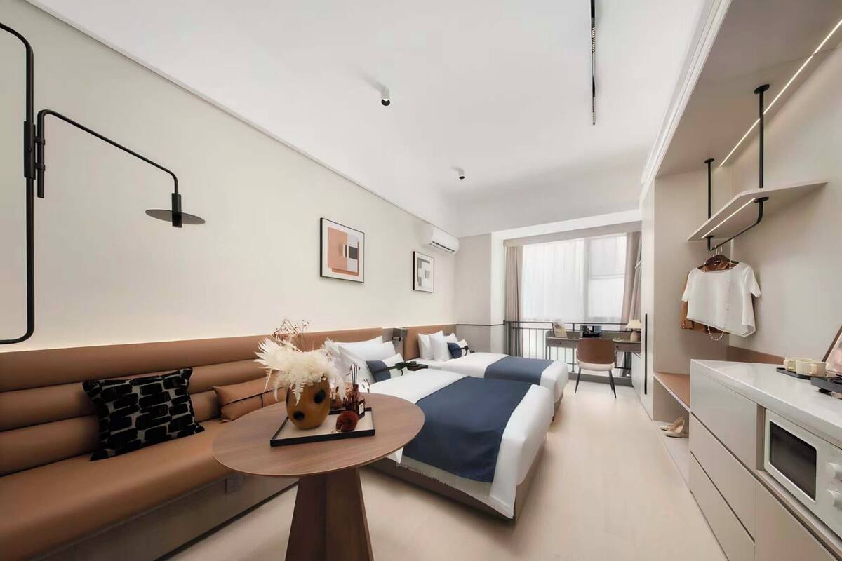 Een moderne hotelkamer met een bank, twee bedden, een bureau en uitzicht op de stad.