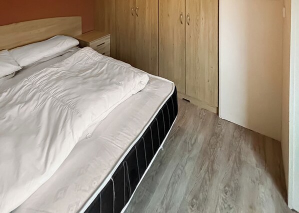 Un letto con biancheria bianca, una testiera in legno, un comodino con cassetti e un armadio a due ante.