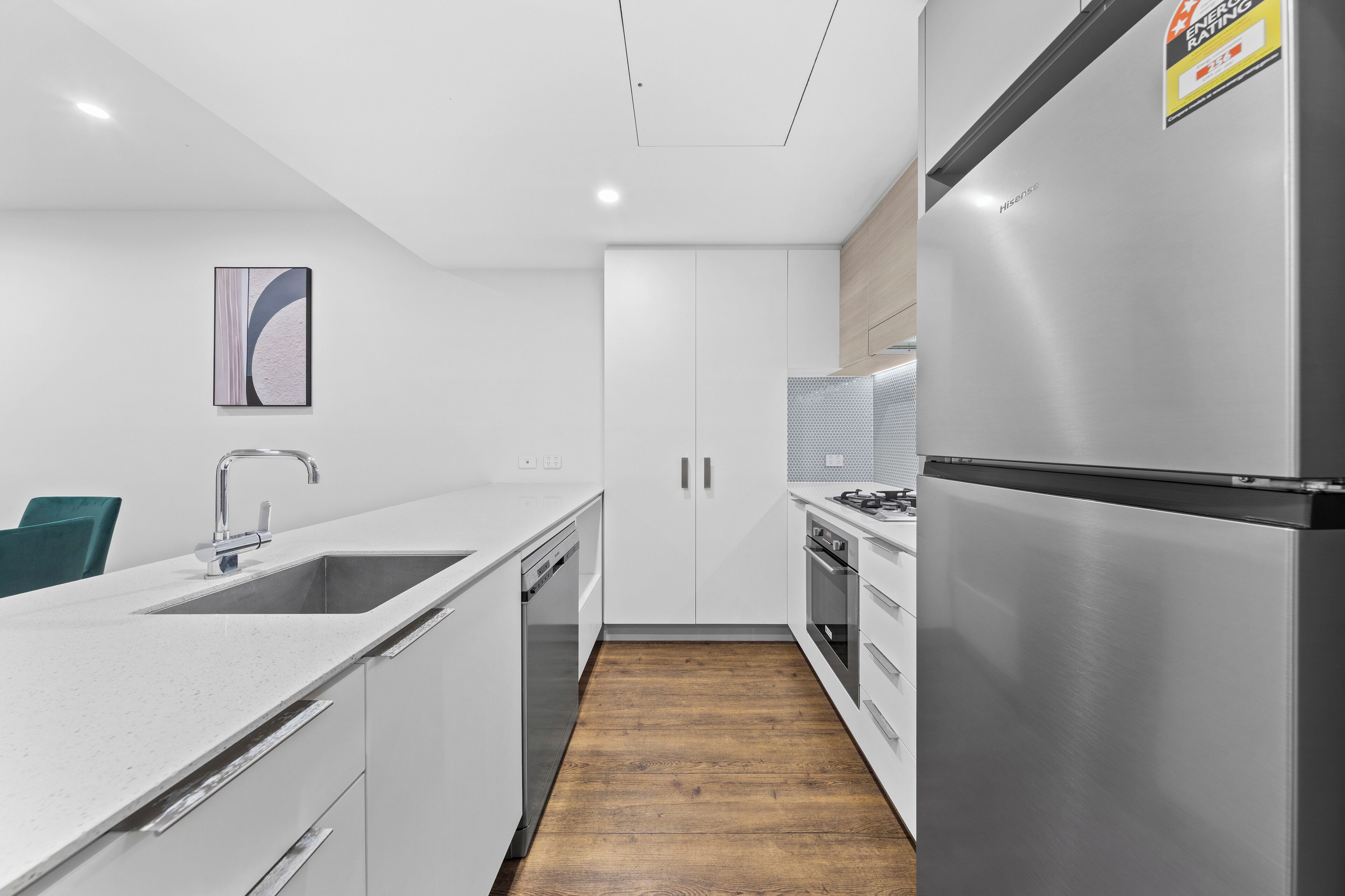 A modern kitchen with white cabinetry, stainless steel appliances, and a wooden floor.