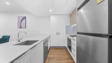 A modern kitchen with white cabinetry, stainless steel appliances, and a wooden floor.