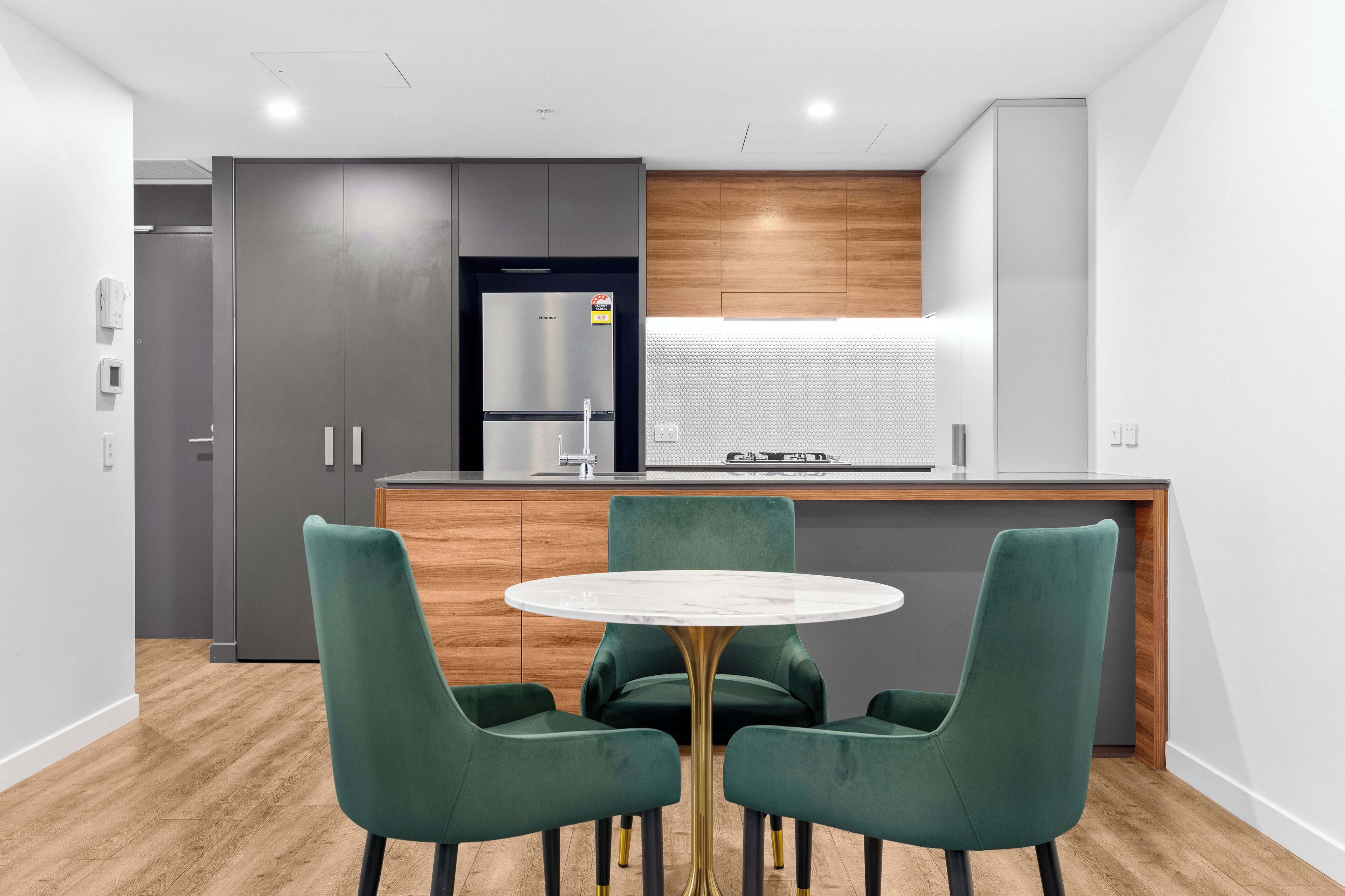 A modern kitchen with a built-in Hisense refrigerator, wooden cabinets, and a marble-top dining table with green upholstered chairs.