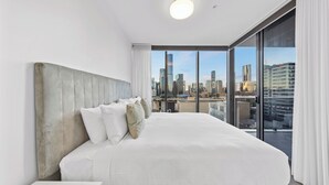 Ein modernes Hotelzimmer mit einem großen Bett, weißer Bettwäsche und Blick auf die Stadt durch raumhohe Fenster.