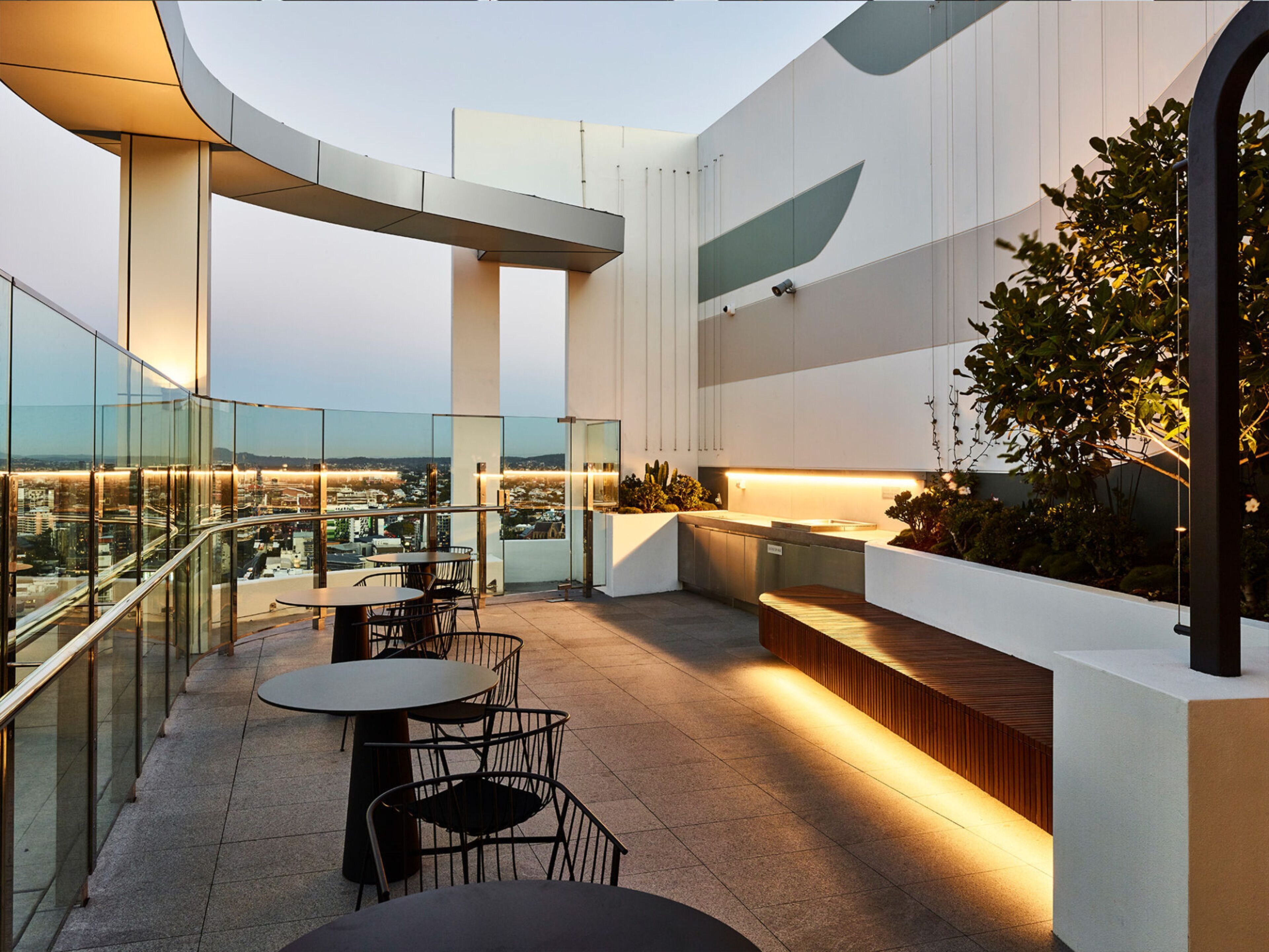 A rooftop terrace with tables and chairs, a bar area, and a view of the cityscape.