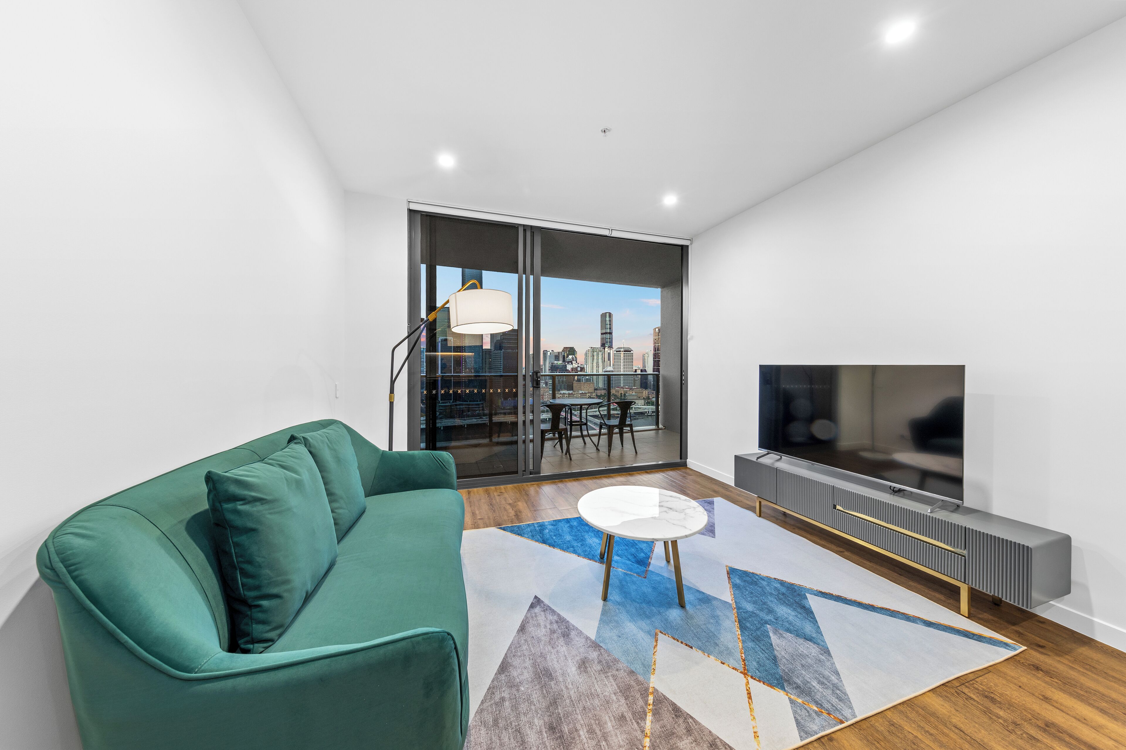 A modern living room with a green sofa, a white coffee table, and a large TV.