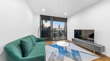 A modern living room with a green sofa, a white coffee table, and a large TV.