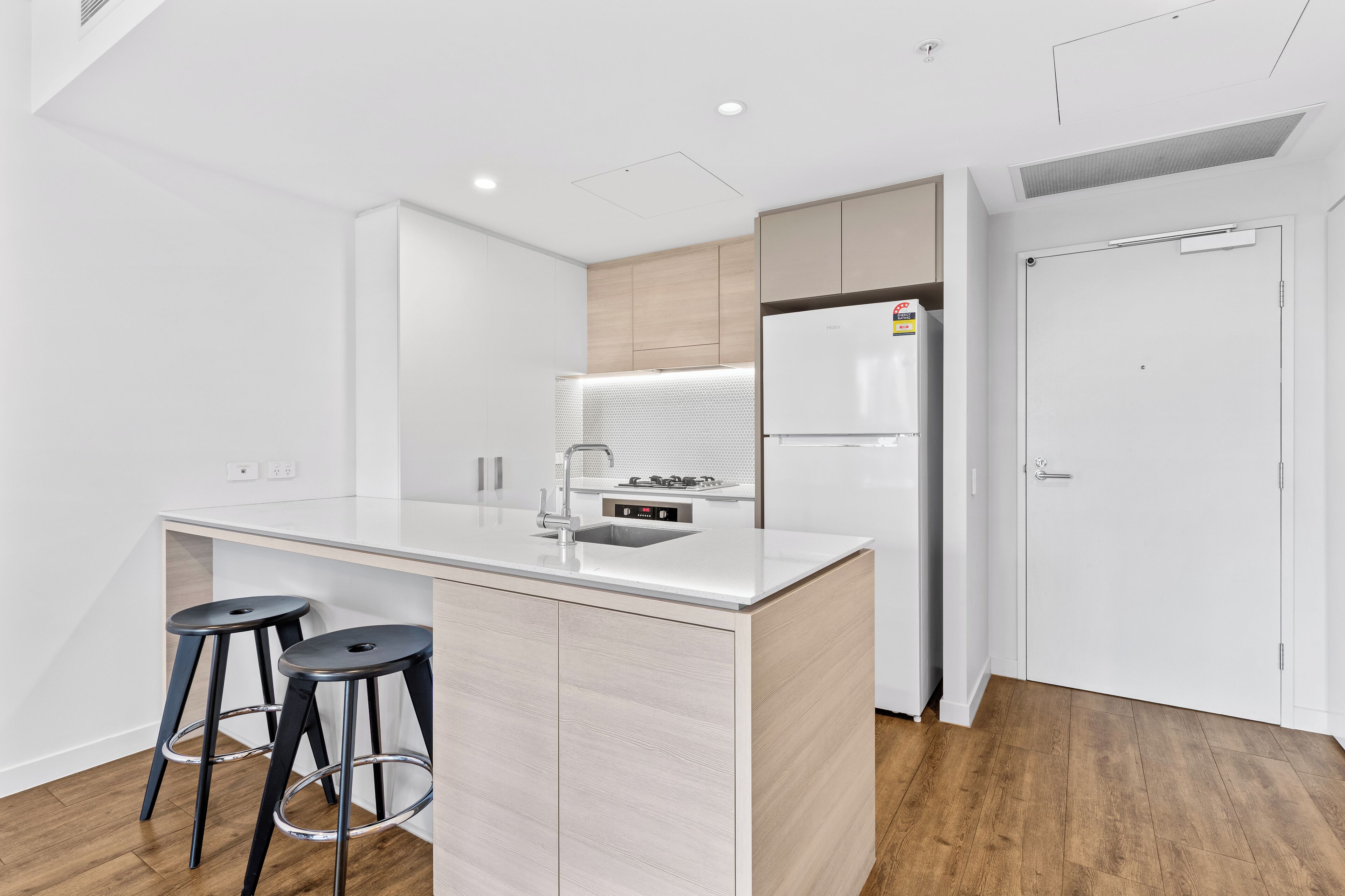 Cozinha moderna com ilha central, banquetas, geladeira e porta dupla.