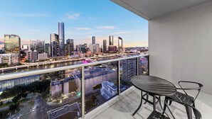 Ein Balkon mit Tisch und Stühlen mit Blick auf eine Stadtlandschaft, die moderne Gebäude und einen Fluss zeigt.