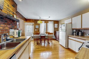 Cozy kitchen with a brick accent wall, sink, stove, refrigerator, dining area, and chandelier.