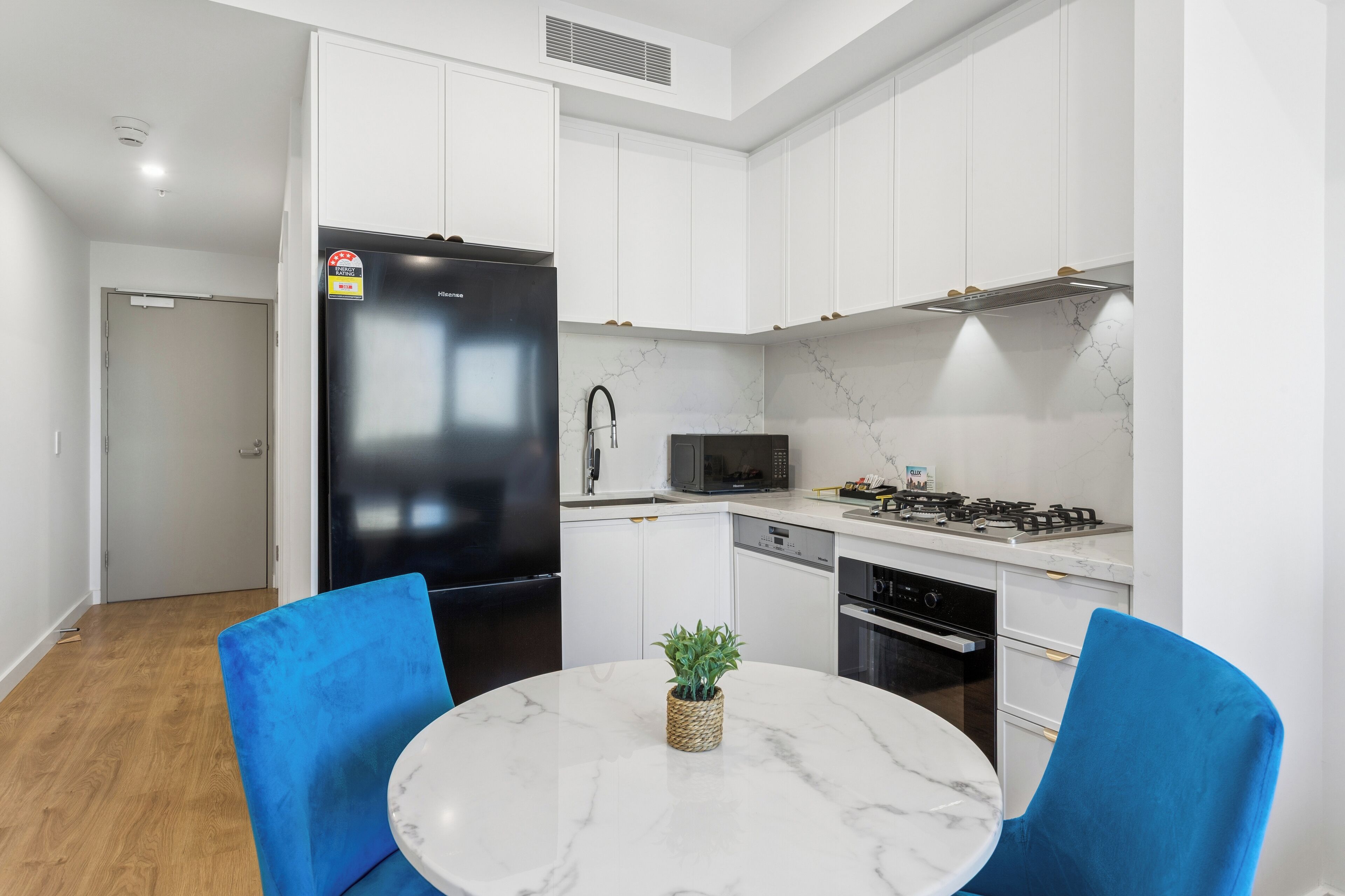 Una cocina moderna con armarios blancos, un refrigerador negro, un microondas, una estufa a gas y una mesa de comedor con sillas azules.