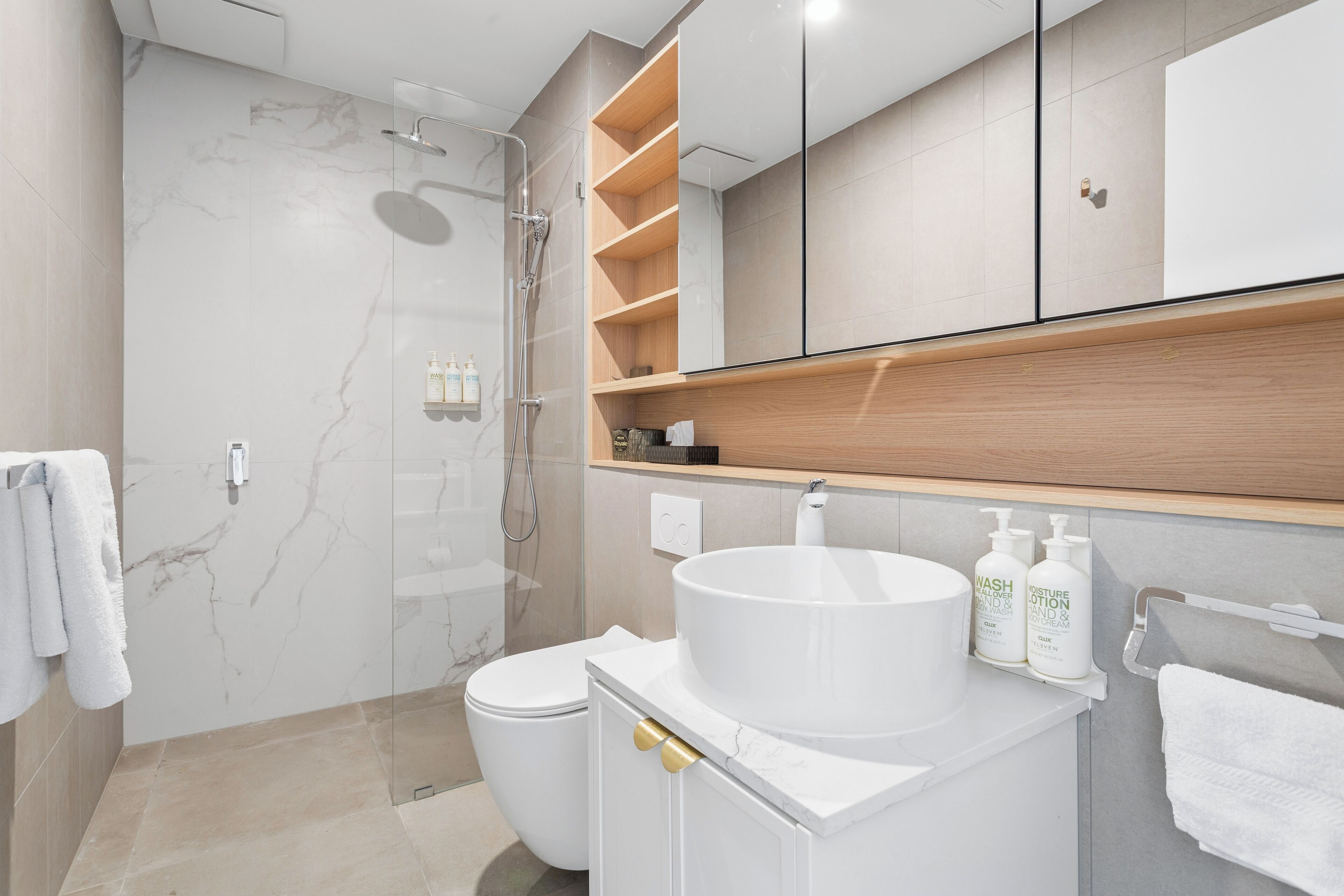 A modern bathroom with a marble wall, a white sink, and a glass-enclosed shower.