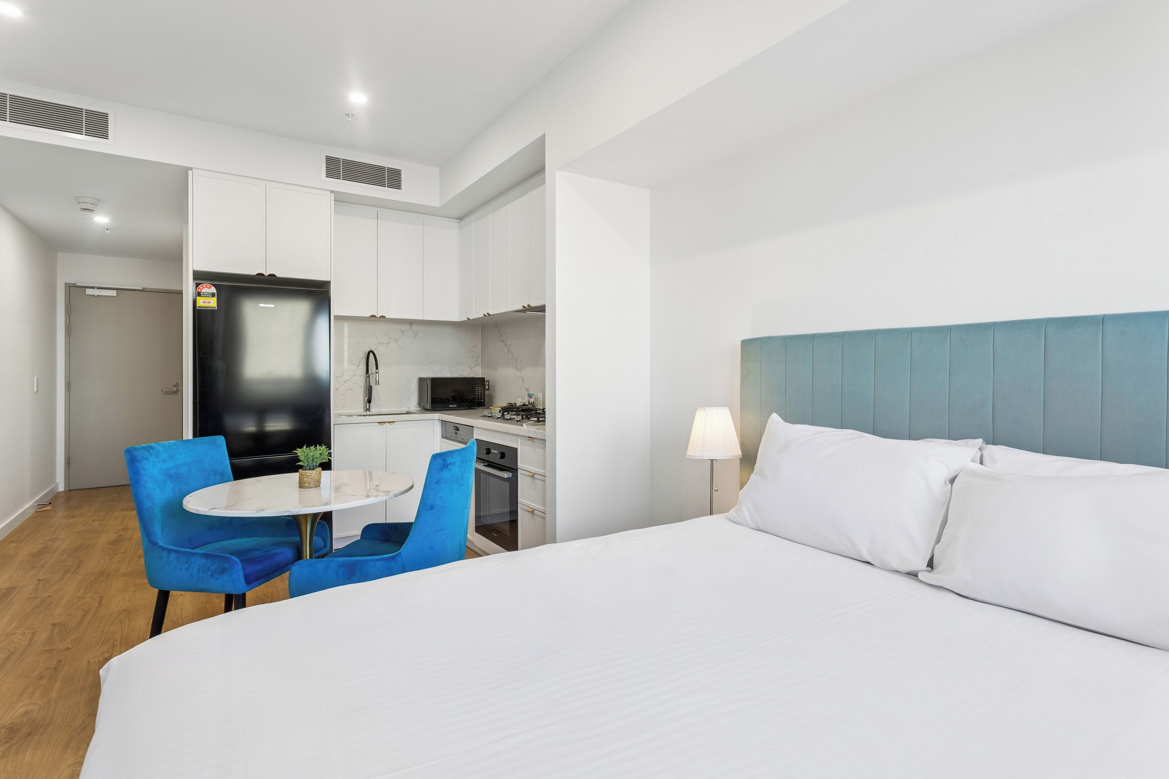 A hotel room with a bed, a desk with a chair, a kitchenette, and a bathroom.