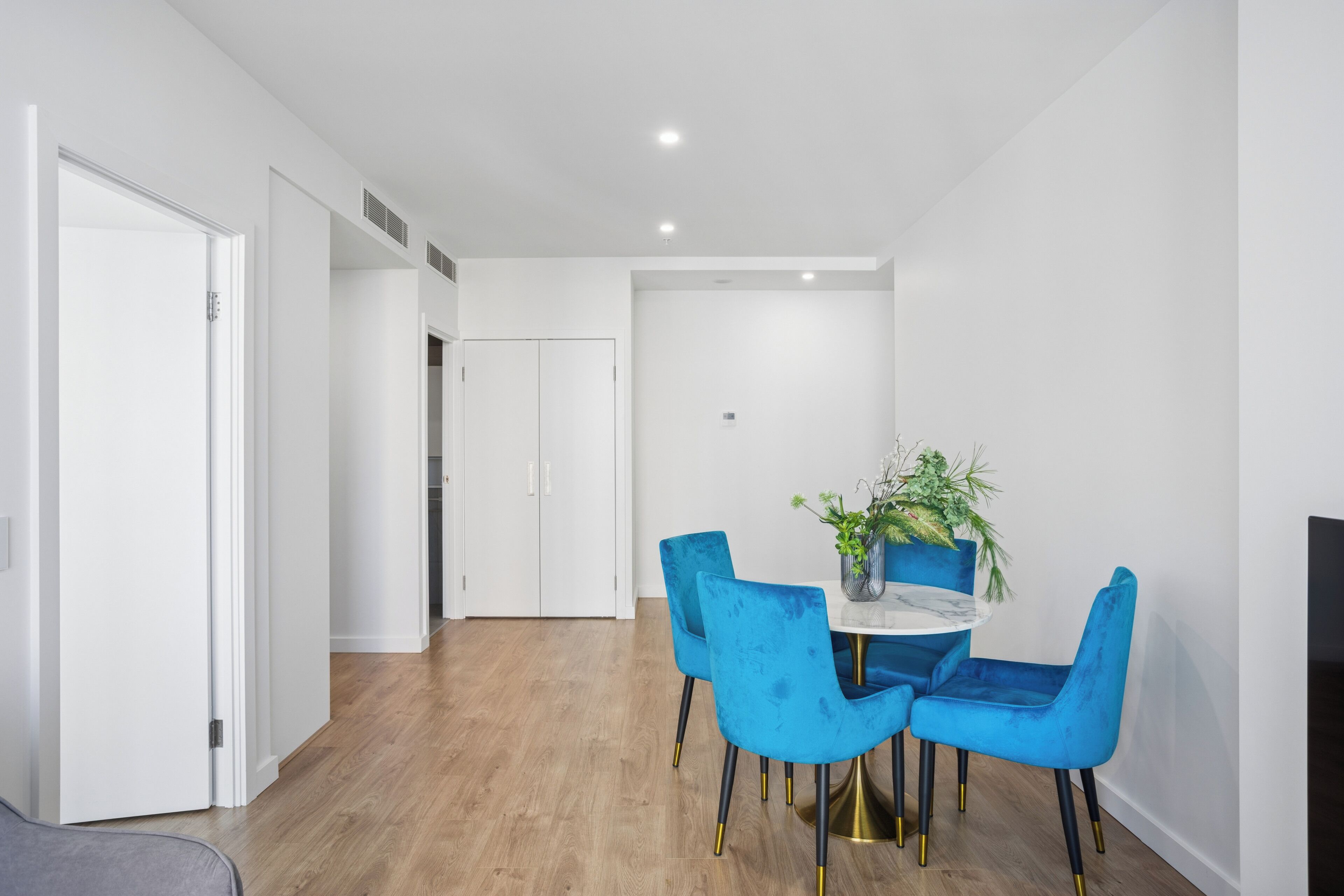 A modern dining area with a round table, blue chairs, and a potted plant.