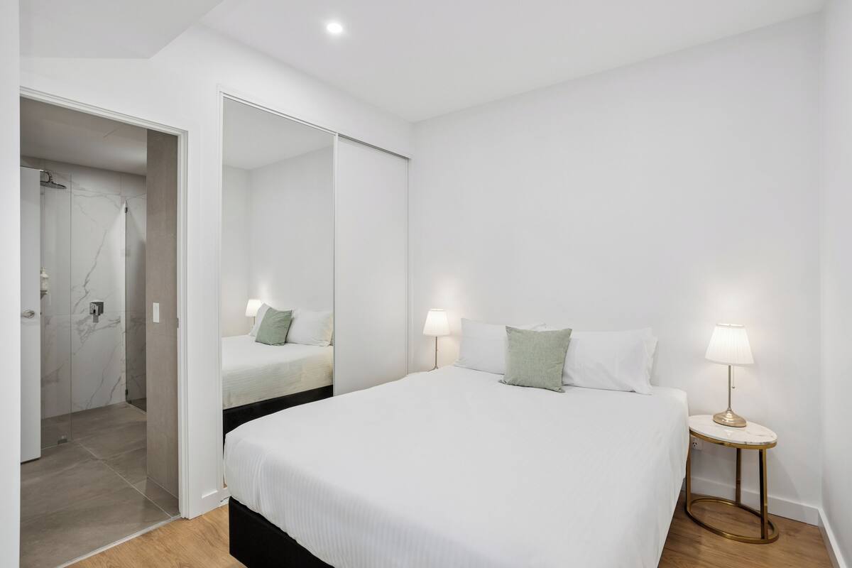 A bedroom with a large bed, bedside lamps, a mirror, and a door leading to a bathroom.