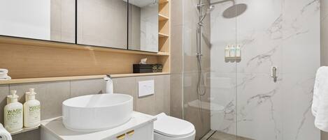 A modern bathroom with a glass-enclosed shower, a white sink, and a toilet.