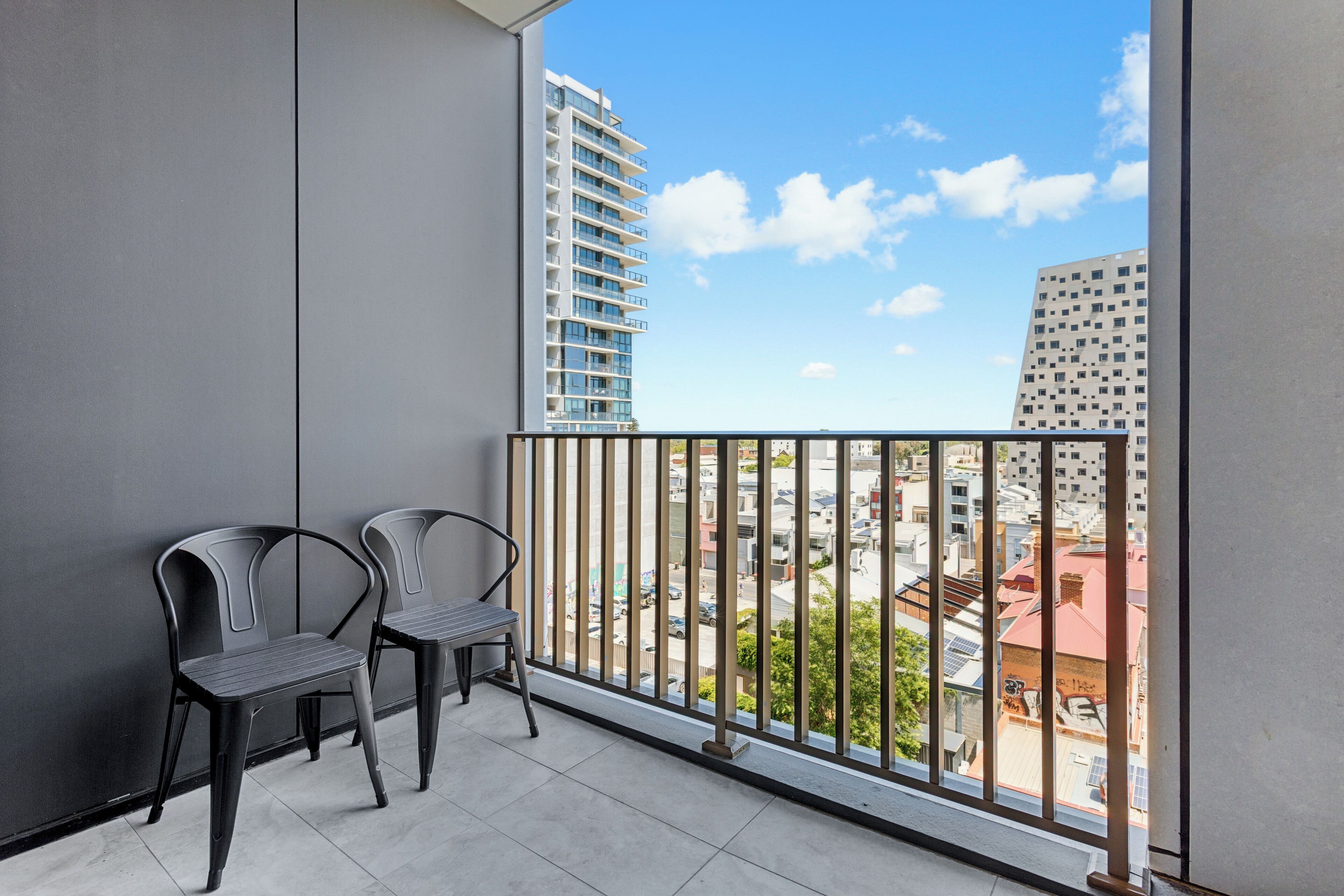 A balcony with two chairs, a view of a cityscape, and a building with balconies.