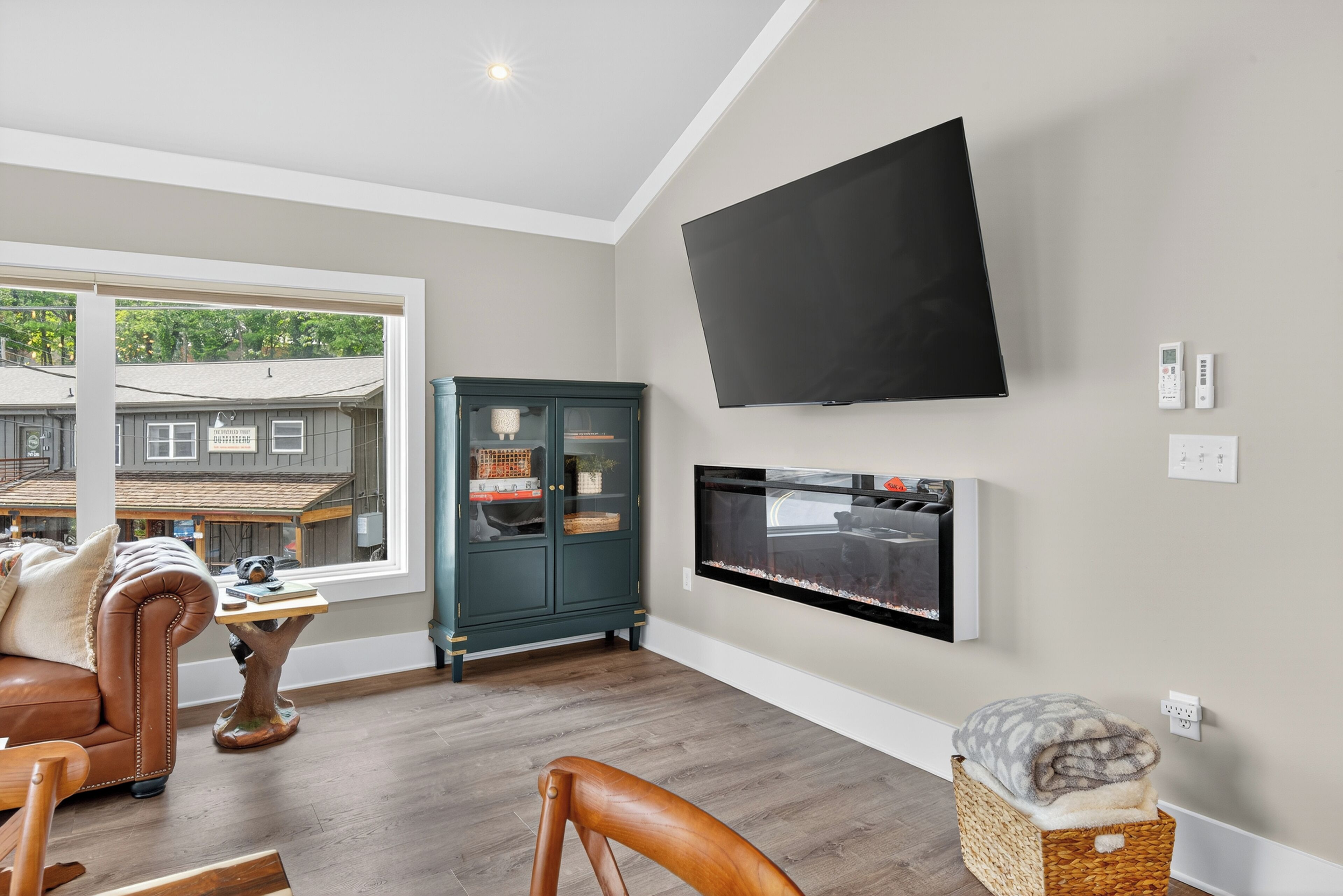 A modern living room with a large flat-screen TV, a fireplace, a comfortable sofa, and a view of the outside.
