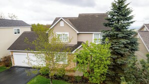 A residential house with a garage, a well-maintained lawn, and a large evergreen tree. - Mountain-View Home with Private Hot Tub, Game Room & Firepit — Sleeps 16 (Somerset)